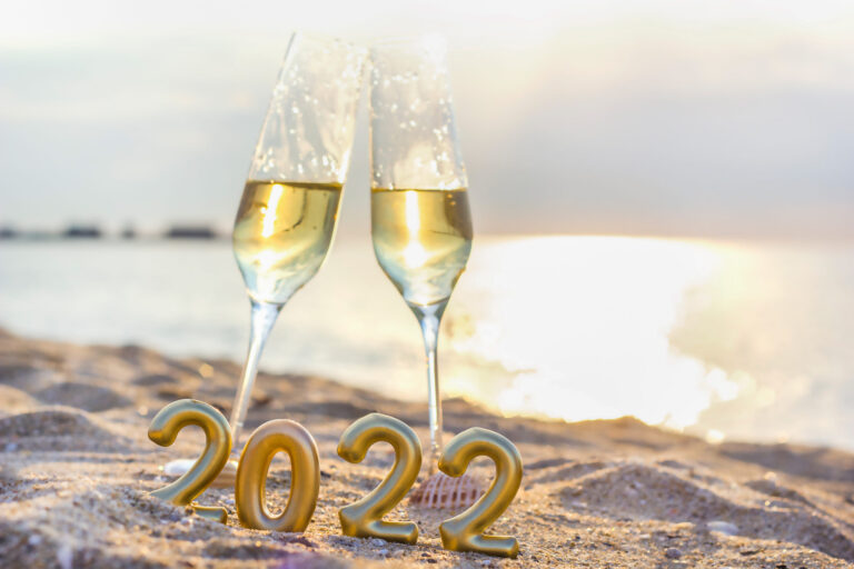 a beach scene with two champagne glasses and mini 2022 balloons.